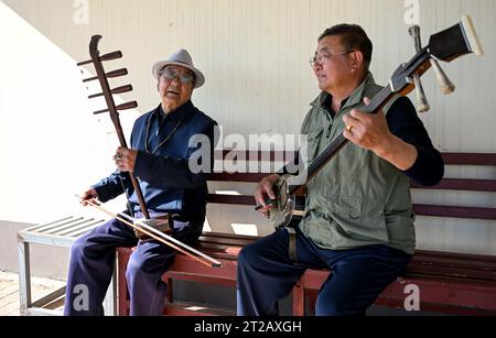 (231018) -- ORDOS, 18. Oktober 2023 (Xinhua) -- Dorji (R) und sein Vater Mingan-erdeni spielen Musik in ihrem Innenhof in Otog Banner of Ordos, nordchinesischer autonomer Region Innere Mongolei, 16. Oktober 2023. Dorji ist ein 61-jähriger Hirte, der in Otog Banner lebt. Während der Herbstsaison gehört Dorjis tägliche Routine zum Hüten von Pferden und Ziegen. Er hat über 200 Arabas Kaschmirziegen, die eine solide wirtschaftliche Rendite bieten. In seiner Freizeit nimmt Dorji mit seinem 91-jährigen Vater Mingan-erdeni an einer lokalen kulturellen Aktivität namens „Nair“ Teil. „Nair“ geht auf die Yuan-Dynastie (1271–1368) zurück Stockfoto
