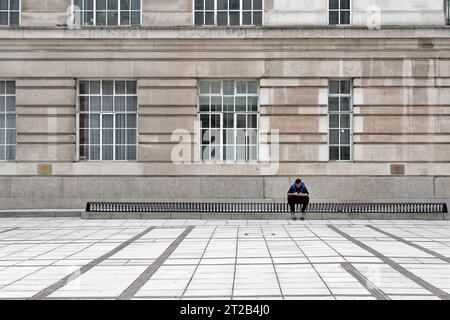 Ein junger Mann, der mit einem Mobiltelefon auf modernen Sitzplätzen in einer düsteren urbanen Landschaft mit brutalistischer grauer Architektur saß, Waterloo London England UK Stockfoto