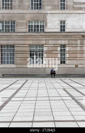 Ein junger Mann, der mit einem Mobiltelefon auf modernen Sitzplätzen in einer düsteren urbanen Landschaft mit brutalistischer grauer Architektur saß, Waterloo London England UK Stockfoto