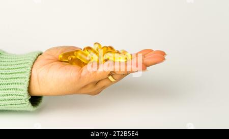 Eine Handvoll Omega-3-reicher Wildlachs- und Fischöl-Kapseln präsentiert auf einem weichen cremeweißen Hintergrund. Stockfoto