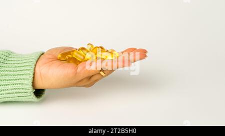 Eine Handvoll Omega-3-reicher Wildlachs- und Fischöl-Kapseln präsentiert auf einem weichen cremeweißen Hintergrund. Stockfoto