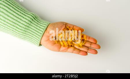 Eine Handvoll Omega-3-reicher Wildlachs- und Fischöl-Kapseln präsentiert auf einem weichen cremeweißen Hintergrund. Stockfoto