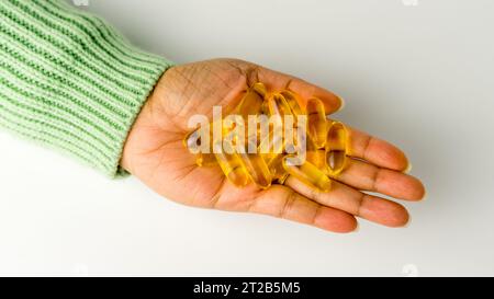 Eine Handvoll Omega-3-reicher Wildlachs- und Fischöl-Kapseln präsentiert auf einem weichen cremeweißen Hintergrund. Stockfoto