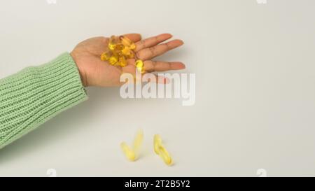 Eine Handvoll Omega-3-reicher Wildlachs- und Fischöl-Kapseln präsentiert auf einem weichen cremeweißen Hintergrund. Stockfoto