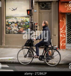 Ein Geschäftsmann wartet auf eine Ampel auf seinem Fahrrad im Viertel Le Marais in Paris, Frankreich. Stockfoto