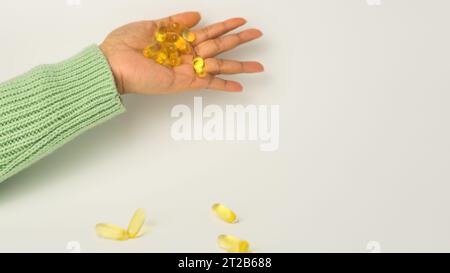 Eine Handvoll Omega-3-reicher Wildlachs- und Fischöl-Kapseln präsentiert auf einem weichen cremeweißen Hintergrund. Stockfoto