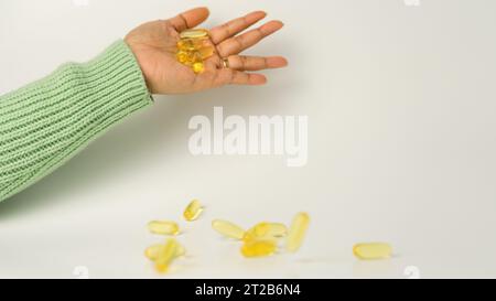 Eine Handvoll Omega-3-reicher Wildlachs- und Fischöl-Kapseln präsentiert auf einem weichen cremeweißen Hintergrund. Stockfoto