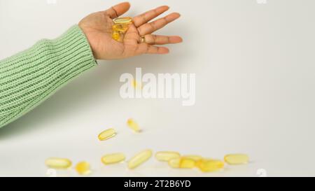 Eine Handvoll Omega-3-reicher Wildlachs- und Fischöl-Kapseln präsentiert auf einem weichen cremeweißen Hintergrund. Stockfoto