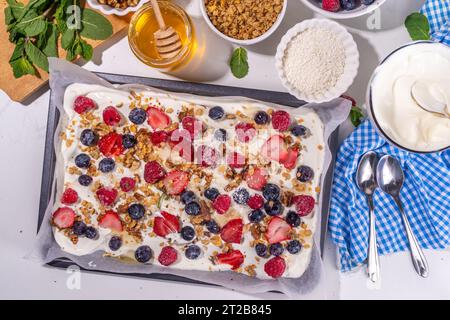 Kochen Herstellen gefrorener Joghurtrinde Hintergrund mit griechischem Joghurt, frischer Beere, Müsli, Honig, Schokoladensauce, mit Backblech Deko. Blick von oben auf die Frau Stockfoto