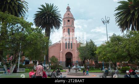 Otavalo, Imbabura / Ecuador - 14. Oktober 2023: Menschen gehen im zentralen Park von Otavalo mit der Kathedrale zwischen den Bäumen im Hintergrund Stockfoto