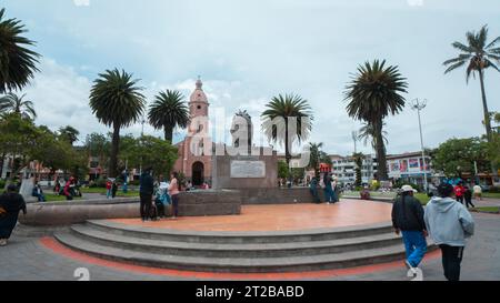 Otavalo, Imbabura/Ecuador - 14. Oktober 2023: Menschen gehen vor dem Ruminahui-Denkmal im zentralen Park von Otavalo mit der Kathedrale Stockfoto