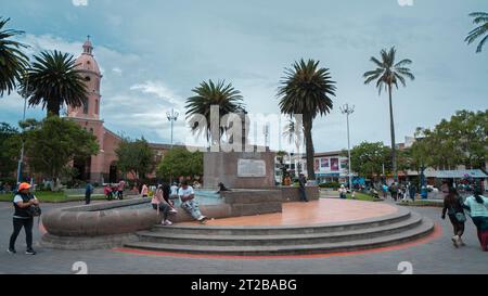 Otavalo, Imbabura/Ecuador - 14. Oktober 2023: Menschen gehen vor dem Ruminahui-Denkmal im zentralen Park von Otavalo mit der Kathedrale Stockfoto