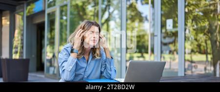 Enttäuschte junge Geschäftsfrau, die sich frustriert fühlte, mit einem Laptop draußen auf der Straße saß, aufschaute und sich beschwerte Stockfoto