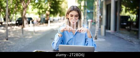 Junge Geschäftsfrau, nehmen an einer Online-Videokonferenz Teil, schreiben, arbeiten, Notizen in ihren Dokumenten machen, draußen an der frischen Luft sitzen Stockfoto