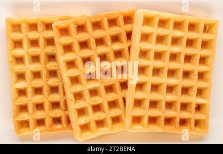 Drei frisch gebackene aromatische Waffeln auf einem weißen Keramikplatte, Makro, Blick von oben. Stockfoto