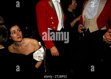 1980er Jahre Hunt Ball im Tysoe Manor feiert das Ende der Jagdsaison. Eine Frau in einem schulterfreien, trägerlosen schwarzen Ballkleid und zwei Masters of Foxhounds plaudern in ihrer traditionellen, pinken Abendkleidung. Tysoe, Warwickshire, England, April 1982. HOMER SYKES AUS DEN 1980ER JAHREN. Stockfoto