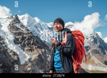 Porträt eines Sherpa-Mannes mit Rucksack, der Walkie-Talkie benutzt, um einen Rettungshubschrauber mit Mera Peak 6476 m Hintergrund zu rufen. Expedition im hohen Himalaya DURIN Stockfoto