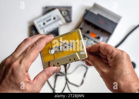 Manuelles Zurückspulen einer Kassette mit Hilfe eines Stifts, eines Kassettenspielers und mehrerer Bänder auf weißem Hintergrund. Stockfoto