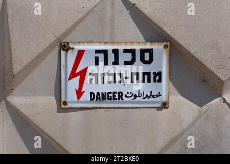 Elektrizitätsgefahr-Schild in Hebräisch, Arabisch und Englisch, an eine Betonwand genagelt Stockfoto