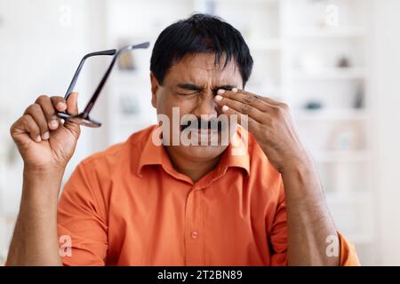Erschöpfter reifer indianer, der Augen reibt und eine Brille hält Stockfoto