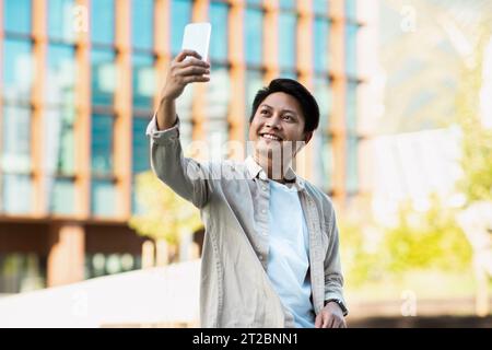 Fröhlicher junger asiatischer Unternehmer, der Selfie auf der Straße macht Stockfoto