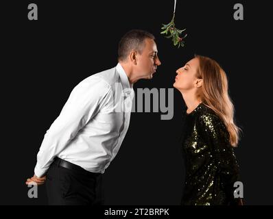 Reifes Paar küsst sich unter Mistelzweig auf dunklem Hintergrund Stockfoto