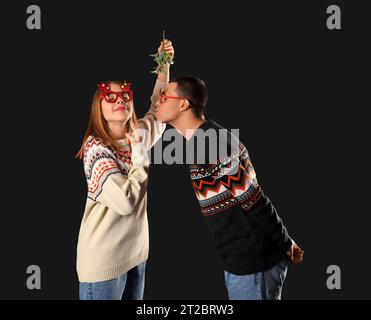 Junges Paar küsst sich unter Mistelzweig auf dunklem Hintergrund Stockfoto