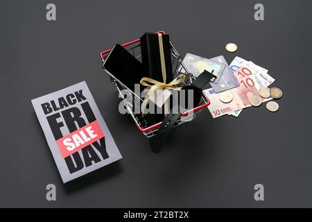 Grußkarte mit Text BLACK FRIDAY SALE, Warenkorb, Geschenke, Kreditkarten und Geld auf dunklem Hintergrund Stockfoto