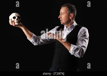 Reifer Schauspieler mit Schädel auf dunklem Hintergrund Stockfoto