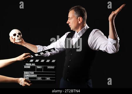 Reifer Schauspieler, der Schädel und Hände mit Klapperbrett auf dunklem Hintergrund hält Stockfoto