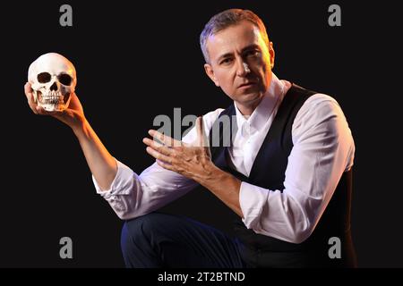 Reifer Schauspieler mit Schädel auf dunklem Hintergrund Stockfoto