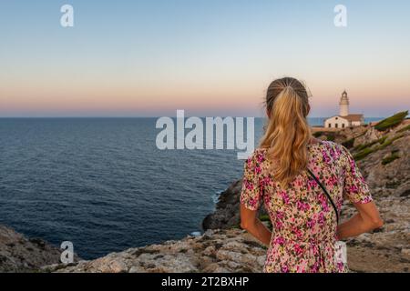 Blondes Mädchen am Leuchtturm von Capdepera mit dem Mittelmeer im Hintergrund in Cala Ratjada auf Mallorca, Spanien Stockfoto