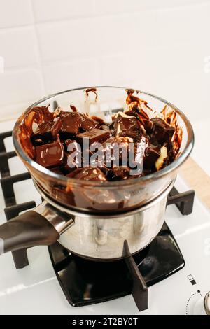 Schokolade und Kakaobutter werden durch Dämpfen in einer Glasplatte geschmolzen, die auf einen Topf mit gekochtem Wasser gestellt wird. Nahaufnahme, Draufsicht. Vertikaler Rahmen. Stockfoto