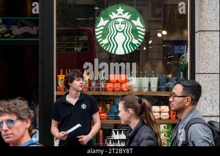 Madrid, Spanien. Oktober 2023. Ein Starbucks-Mitarbeiter steht vor der multinationalen amerikanischen Kaffeekette, während Fußgänger in Spanien an ihr vorbeilaufen. Quelle: SOPA Images Limited/Alamy Live News Stockfoto
