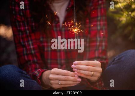 Strahlender Glitzer brennt in Frauenhänden. Mädchen in rotem kariertem Hemd lächelt. Atmosphäre von Weihnachten, Neujahr. Lustig, Urlaubsdekor. Stockfoto