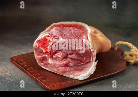 Roher Achsschenkel. Frische, rohe Eisbein-Schweinshaxe auf einer handgefertigten Tonplatte. Schwarzer Holzhintergrund. Stockfoto