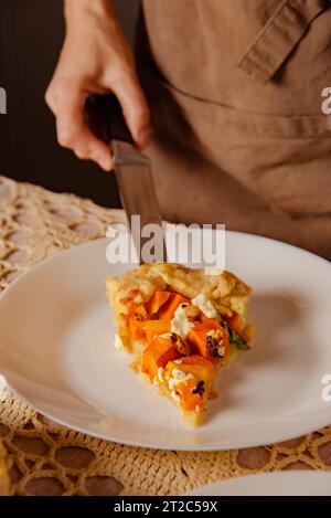 Nahaufnahme weiblicher Hand legt veganen Kürbiskuchen zum Abendessen auf weißen Teller Stockfoto