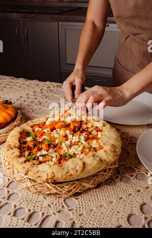 Frau breitet frisch gebackenen Kürbiskuchen auf Tellern in gemütlichem Haus aus. Herzhafter Kuchen Stockfoto