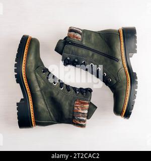 Dunkelgrüne Damenstiefel auf weißem Holzhintergrund. Draufsicht, flach. Trendige Freizeitschuhe, Konzept der Werbung Herbst- oder Winterschuhe Sale Shop. Stockfoto