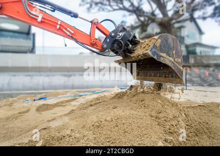 Bulldozer gräbt Sand an einem Sandstrand. Strandhäuser und Betonmauern am Strand. Auckland. Stockfoto