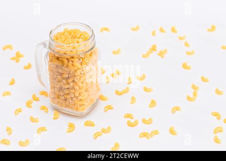 Ungekochte Chifferi Rigati Pasta in Glasglas auf weißem Hintergrund. Fett und ungesunde Lebensmittel. Verstreute Klassische Trockene Makkaroni. Italienische Kultur und Küche. Rohe Pasta Stockfoto
