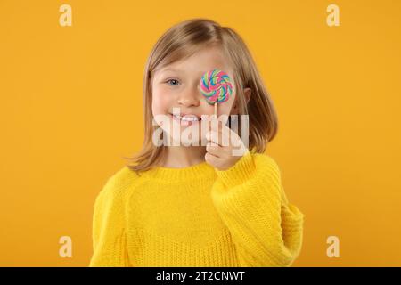Porträt eines glücklichen Mädchens mit Lutscher auf orangem Hintergrund Stockfoto