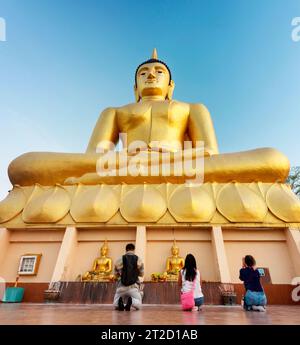 Sie verehren das wunderschöne, lebendige Goldbild des Buddha, während die Sonne hinter sich untergeht, eine beliebte heilige Stätte und Touristenattraktion mit Blick auf Pakse und die Stockfoto