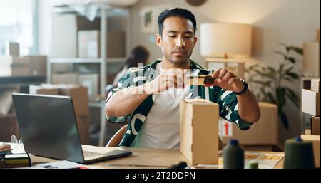 Asiatischer Mann, Telefon und Box in der Logistik oder in kleinen Unternehmen zur Bestandskontrolle oder Preisgestaltung für E-Commerce. Männliche Person oder Ladenbesitzer mit Handy Stockfoto