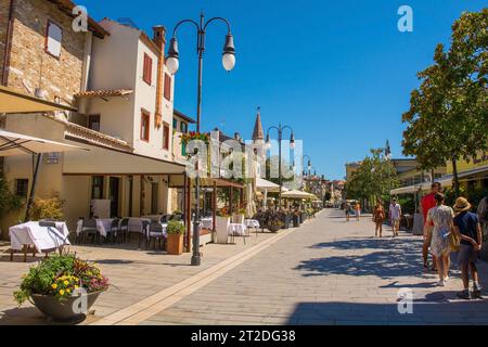 Grado, Italien - 11. August 2023. Eine der wichtigsten Fußgängerstraßen, gesäumt von Bars und Restaurants, im historischen Zentrum von Grado, an der Küste von N.E. Italien Stockfoto