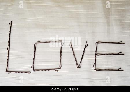 Schreib eine Liebe, geschrieben von Haarnadelpingern, auf beigefarbenem Hintergrund. Das Wort Liebe besteht aus weiblichen Ornamenten. Stockfoto