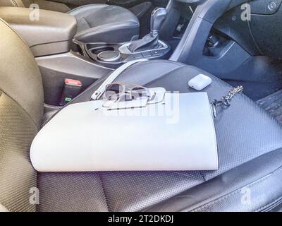 Die wunderschöne, modische Ledertasche und Sonnenbrille mit kabellosen Kopfhörern für weiße Frauen liegen auf dem Ledersessel eines teuren Autos. Stockfoto