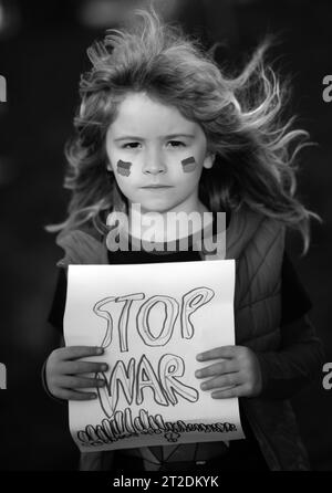 Kind Junge hält Schild mit Worten Stoppt den Krieg im Freien stehen. Kind trägt ein Schild Krieg stoppen. Putin greift das ukrainische Volk an. Stockfoto