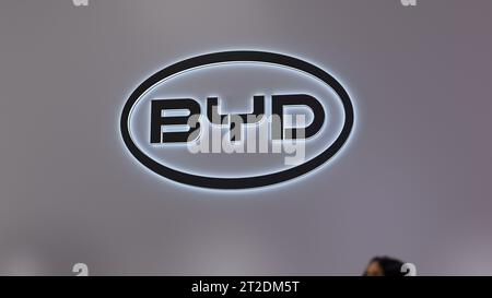 Das Logo von BYD an der Wand des Innengeschäfts. Die Marke BYD Company in einem elektronischen Ausstellungsraum. Ein Teil eines unscharfen Passanten im Vordergrund. Stockfoto