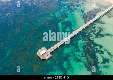 Aus der Vogelperspektive auf einen langen schmalen Steg über einer flachen Küstenbucht mit felsigen Riffen bei Queenscliff auf der Bellarine Peninsula in Victoria, Australien Stockfoto